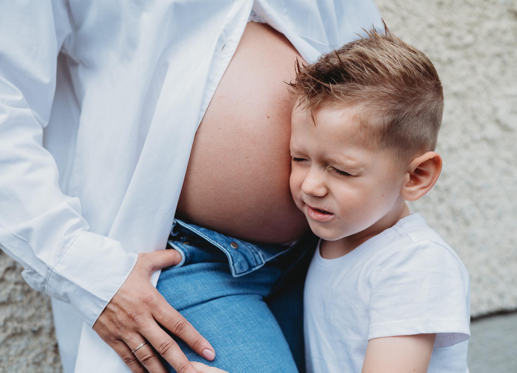Babybauch-Schwangerschaftsshooting in Wien - Kleiner Junge hört am Babybauch von Mama und kneift die Augen zu