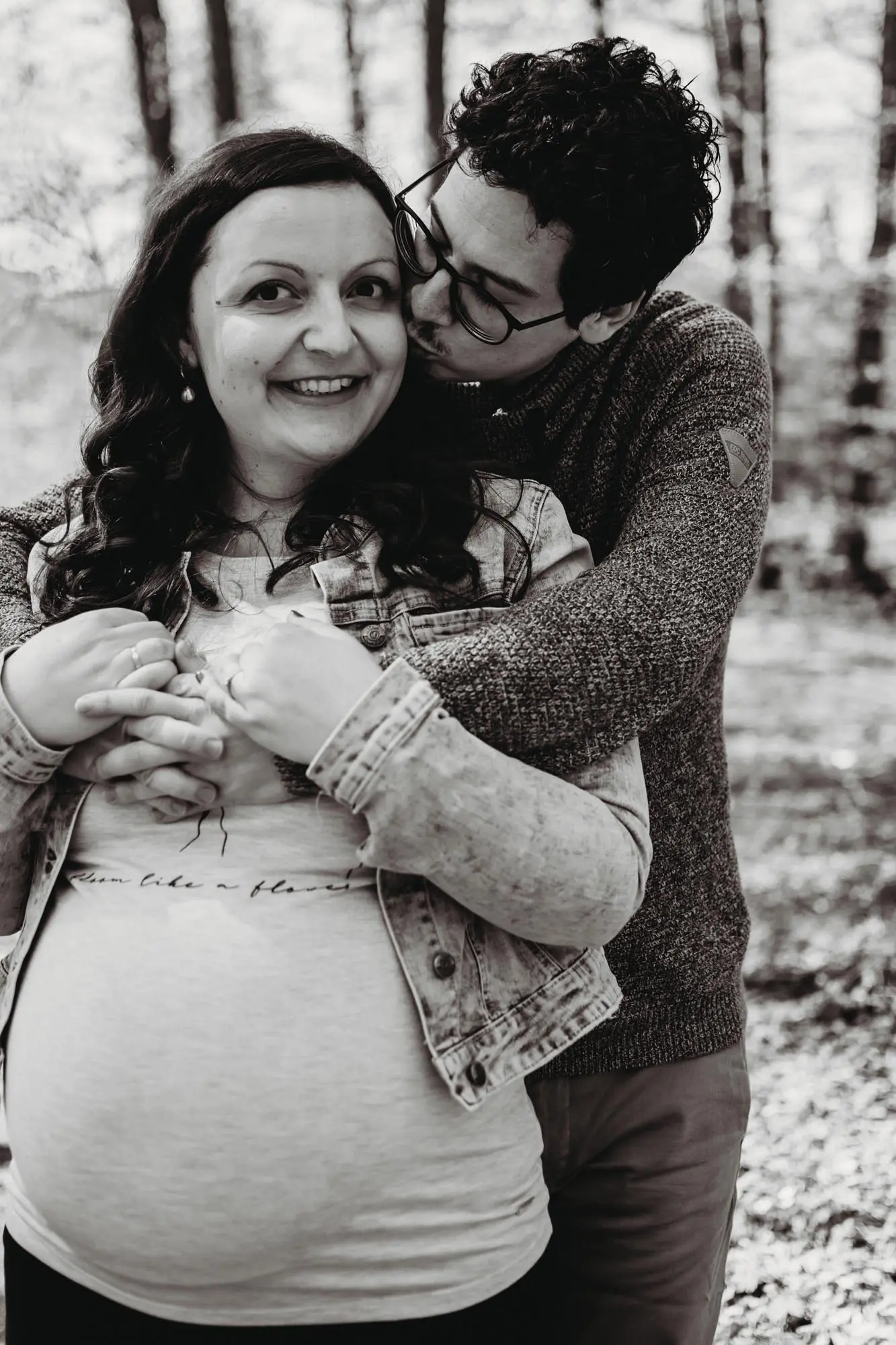 Babybauchshooting: Papa umarmt Mama von hinten und gibt ihr ein Küsschen auf die Wange