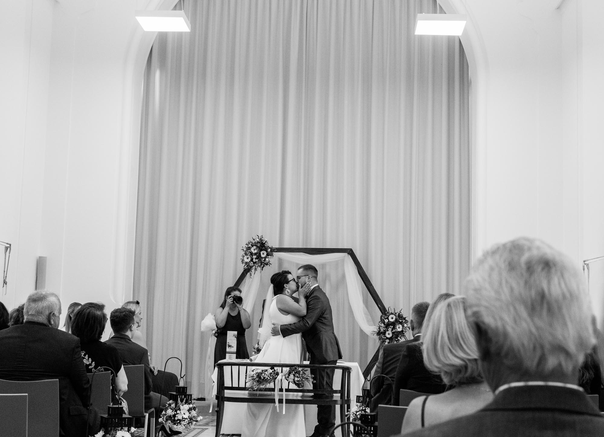 Hochzeitsfotos_Hochzeitsreportage in Wien_Trauung_Brautpaar küsst sich_Aufnahme aus den Gästereihen