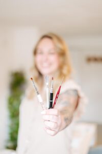 Businessreportage: Nageldesignerin hält ihr Werkzeug in die Kamera (verschiedene Pinsel und Schieber)