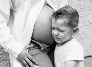 Großer Bruder hört mit geschlossenen Augen am Babybauch der Mama