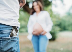 Nahaufnahme auf ein Ultraschallbild. Der Papa hat es in seiner hinteren Hosentasche und im unscharfen Hintergrund sieht man die schwangere Mama und ihren Babybauch