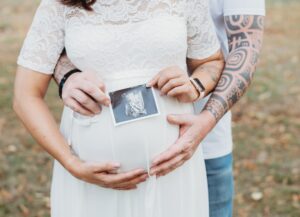Papa und Mama halten das Ultaraschallbild vor den Bauch und umarmen gleichzeitig den Babybauch