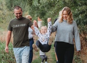 Mama und Papa spielen das Engelchen-Spiel. Sie haben ihre Tochter in der Mitte an der Hand und lassen sie in die Luft fliegen.