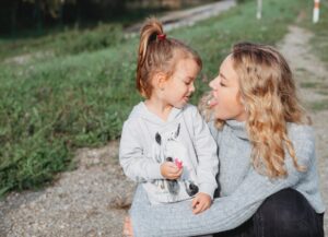 Mama und Tochter die nebeneinander knien und sich die Zunge mit PEZ Zuckerl zeigen