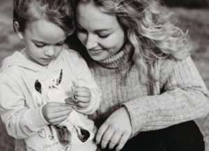 Mama beugt sich zur Tochter und beide packen gemeinsam ein Zuckerl aus