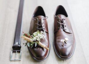Aufnahme der Bräutigam-Accessoires. Braune Lederschuhe, Manschettenknöpfe, Ansteckblume und Gürtel sind wunderschön vorbereitet