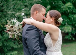 Hochzeitsfotografie, Brautpaarfotos - Braut schlingt die Arme um ihren Bräutigam, der Brautstrauß liegt hinter der Schulter des Bräutigams und die beiden genießen mit geschlossenen Augen und Nase an Nase diesen Moment