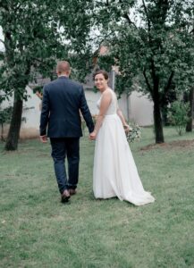 Braupaar geht auf einer Wiese entlang - Perspektive von hinten aufgenommen und nur die Braut dreht sich um