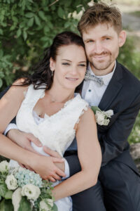 Braut und Bräutigam sitzen auf einer Bank. Die Braut lehnt sich an ihren Ehemann, während er sie umarmt