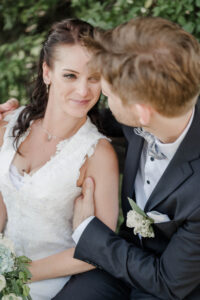 Braut und Bräutigam sitzen auf einer Bank. Die Braut strahlt ihren Mann an