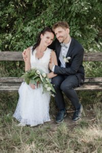 Braut und Bräutigam sitzen auf einer Bank, lehnen die Köpfe aneinander und er Bräutigam umarmt und hält seine Braut