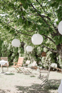 Bild der Location mit Holzstühlen unter einem mit weißen Lampions geschmückten Baum