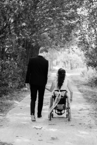 Aufnahme von hinten. Braut und Bräutigam gehen einen Waldweg entlang. Braut und Bräutigam schauen sich verliebt an. Schwarz/weiß Aufnahme