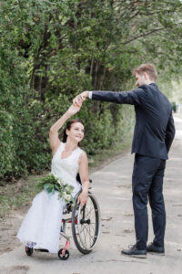 Der Bräutigam dreht seine Ehefrau im Rollstuhl tanzend auf einem Waldweg