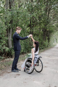 Der Bräutigam dreht seine Ehefrau im Rollstuhl tanzend auf einem Waldweg