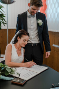 Die Braut unterschreibt die Trauungsurkunde und strahlt dabei