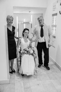 Brautmutter und Brautvater stehen mit ihrer Tochter als Braut im Eingang zum Trauungssaal und begleiten sie zu ihrem zukünftigen Ehemann. Alle strahlen sichtlich