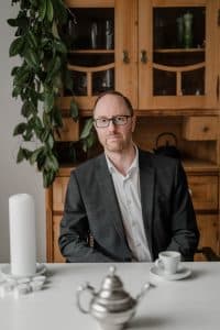 Portrait des Goldschmieds im Rahmen einer Businessreportage in Wien. Er sitzt am Esszimmertisch - vor ihm eine Tasse Kaffe und er schaut seriös in die Kamera