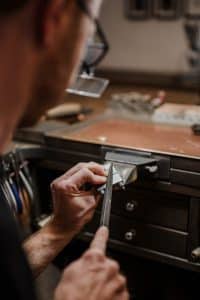 Nahaufnahme eines Goldschmieds während der Arbeit. Der Goldschmied schleift ein Stück Metall auf der Werkbank