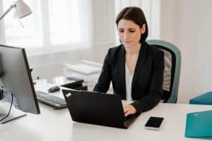 Portrait einer Anwältin, die an ihrem Schreibtisch arbeitet. Sie schaut in ihren Laptop und tippt. Am Schreibtisch ist sonst noch Büroausstattung zu sehen.