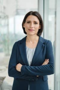 Portrait einer Anwältin im Rahmen einer Businessreportage in Wien. Sie steht an einer Fensterfront und lehnt sich ganz leicht an das Fenster. Dabei schaut sie mit leicht verschränkten Armen direkt in die Kamera