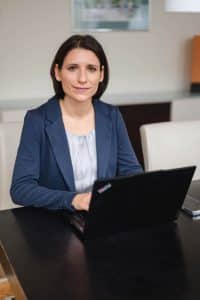 Portrait einer Anwältin im Rahmen einer Businessreportage in Wien. Sie sitzt mit ihrem Laptop am Tisch und schaut in die Kamera