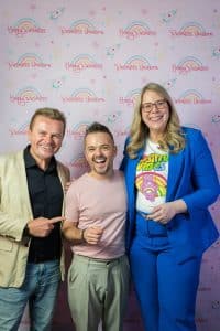 Buinessreportage_Veranstaltungsreporte: Live Video Podcast von Corinna Hintenberger mit Stefan Verra im socialhub Wien. Corinna Hintenberger und Stefan Verra machen im Anschluss an die Veranstaltung mit den Zuschauer*innen noch Fotos vor einer Fotowand - alle lachen herzlich in die Kamera