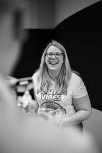 Buinessreportage_Veranstaltungsreporte: Live Video Podcast von Corinna Hintenberger mit Stefan Verra im socialhub Wien. Stimmungsaufnahme der Veranstaltung vor Start der Veranstaltung. Schwarz/Weiß-Aufnahme von Corinna die grad noch eine Story für instagram aufnimmt und dafür von ihrem Geschäftspartner Daniel Zieser aufgenommen wird. Sie lacht herzlich in die Kamera